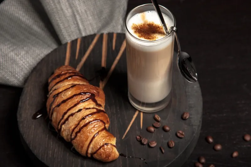 A chocolate-drizzled croissant beside a glass of latte