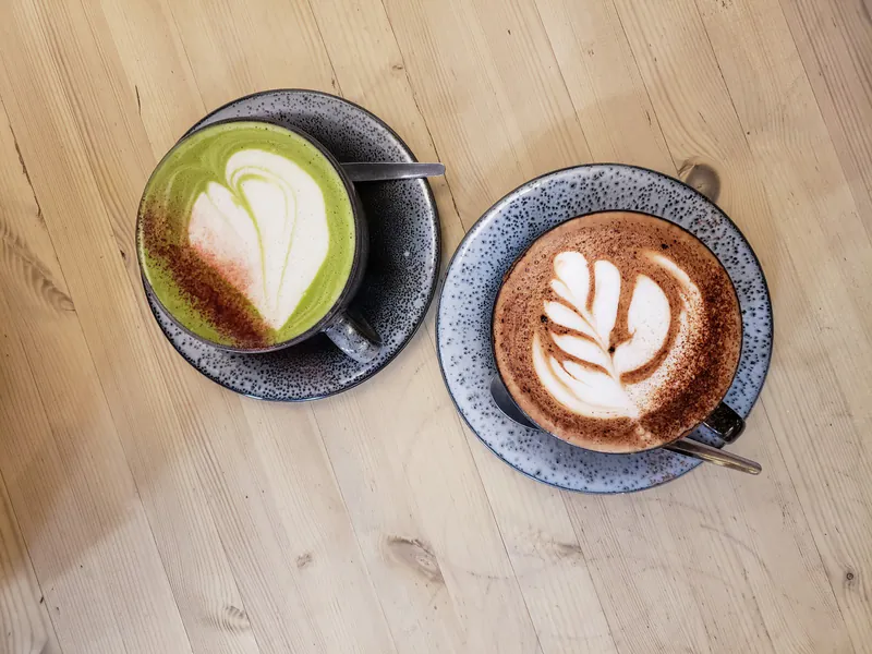 A matcha latte and a mocha side by side on a wooden table